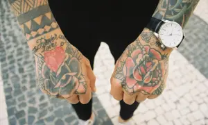 Dłonie pokryte kolorowym tatuażem tradycyjnym: róże, serce i napis "Forever Love". Na lewej ręce zegarek.