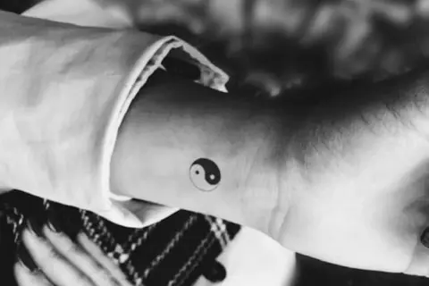 Mały tatuaż yin yang na nadgarstku. Symbolizuje równowagę i harmonię, a jego znaczenie jest głębokie.