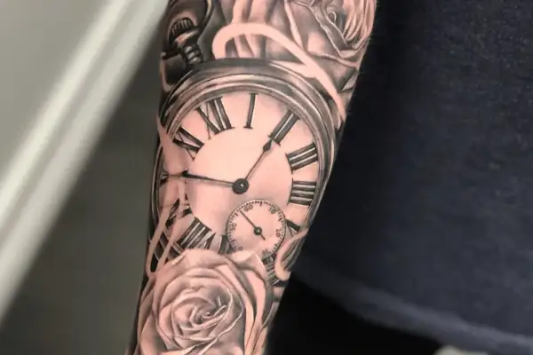 Tatuaż na ramieniu przedstawia kieszonkowy zegar z rzymskimi cyframi i róże. Symbolizuje, że tatuaż czas przemija.